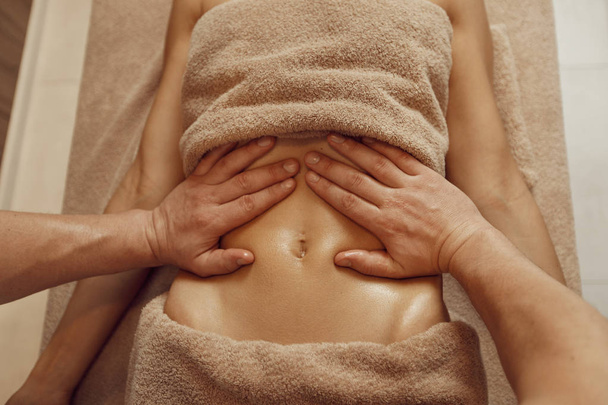 Um massagista mimando o estômago para a jovem mulher em toalha, massagem profissional. Massagem e relaxamento, cuidados com o corpo e a pele. Senhora atraente no salão de spa - Foto, Imagem