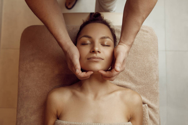 Mãos massagistas masculinas esfregando o rosto para a mulher jovem, vista superior, massagem profissional. Massagem e terapia de relaxamento, cuidados com o corpo e a pele. Senhora atraente no salão de spa
 - Foto, Imagem
