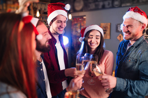 Friends celebrating new year's together. Portrait of Friends With Drinks Enjoying Cocktail Party. Young people laugh. Group of beautiful young people in Santa hats. Blur Background. - Foto, imagen