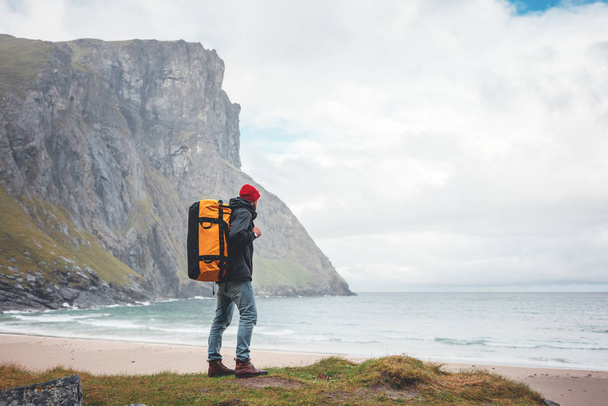 Ember életmód utazó hátizsák túrázás között ködös hegyek az óceán homokos. Egyedül bátor férfi turista áll szemben ord tenger és a nagy hegyi szikla. Vándorlási vágy kaland - Fotó, kép