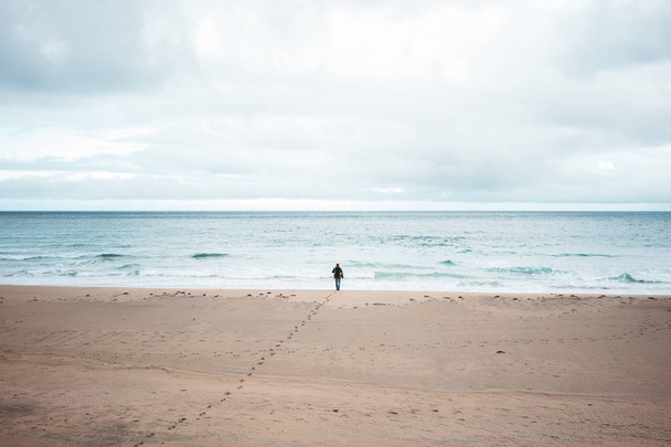 Alone tourist with backpack walks along a deserted beach to the ocean. Nord melancholic nature. Wilderness wanderlust adventure - Fotoğraf, Görsel