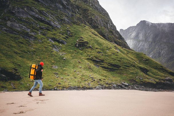 山の中で海の砂の上にバックパックハイキングと一人勇敢な観光客。旅行者は大きな山の岩の前で海のビーチを歩く。ライフスタイル旅行の冒険 - 写真・画像