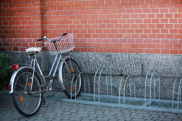 Велосипед, стоящий один на парковке на фоне кирпичной стены
 - Фото, изображение