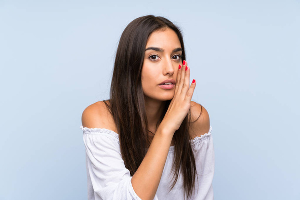Young woman over isolated blue background whispering something - Foto, afbeelding