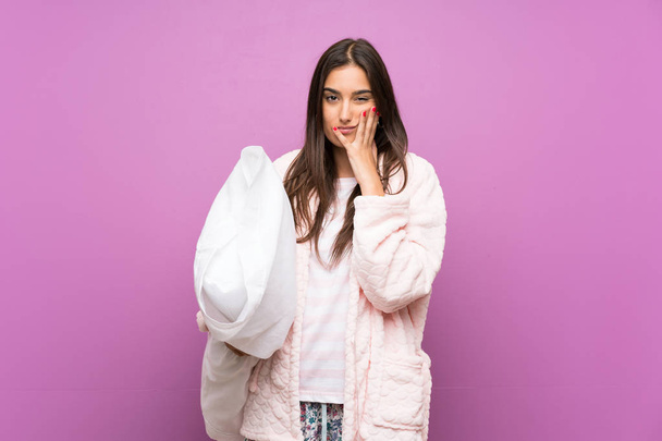 Young woman in pajamas and dressing gown over isolated purple background unhappy and frustrated - Photo, Image