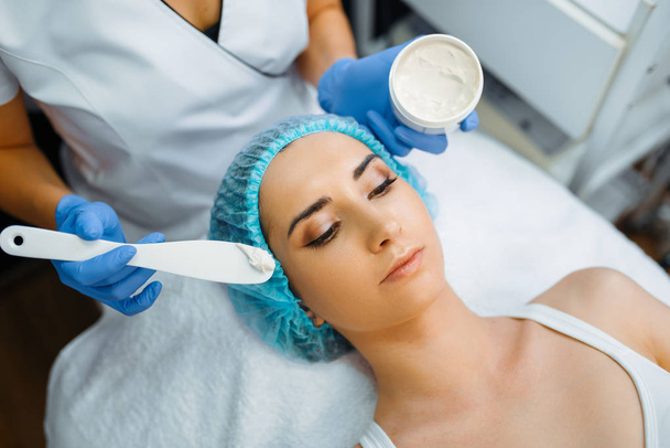 Kozmetik uzmanı kremi kadın hastanın yüzüne sürüyor, botoks hazırlıyor. Güzellik salonunda gençleştirme prosedürü. Doktor ve kadın, kırışıklıklara ve yaşlanmaya karşı estetik ameliyat. - Fotoğraf, Görsel