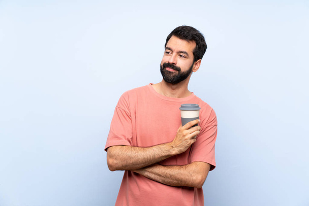 Young man with beard holding a take away coffee over isolated blue background portrait - Photo, image