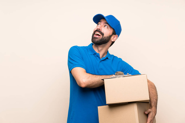 Delivery man with beard over isolated background looking up while smiling - Photo, Image