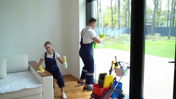 young woman nd man from cleaning service dressed in workwear and rubber gloves dancing in house - Кадры, видео