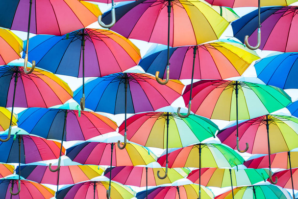 eine Kollektion offener Schirme, die in der Luft schweben, jeder Schirm ist in allen Farben des Regenbogens bemalt, fotografiert von unten - Foto, Bild