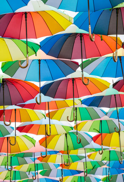eine Kollektion offener Schirme, die in der Luft schweben, jeder Schirm ist in allen Farben des Regenbogens bemalt, fotografiert von unten - Foto, Bild