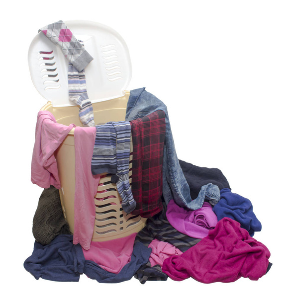 Plastikowy kosz na pranie z otwartą pokrywą, wypełniony różnymi ubraniami, który losowo wystaje z kosza, a także rozrzucone ubrania na podłodze na białym tle - Zdjęcie, obraz