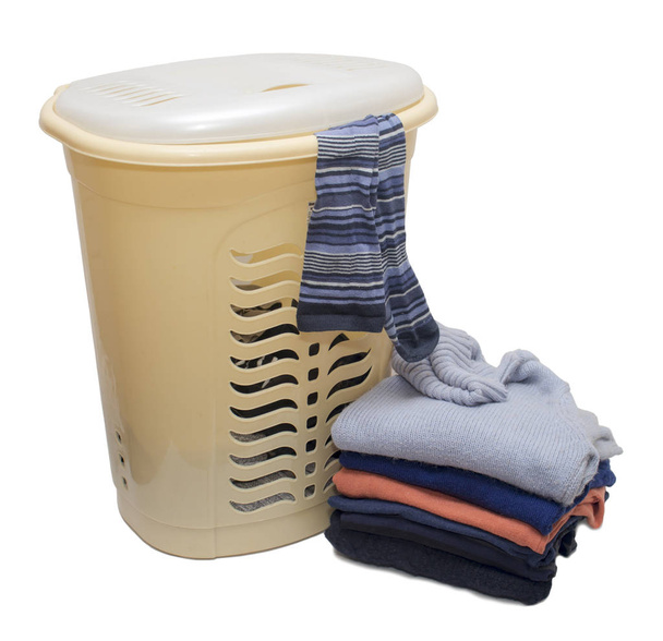 Una cesta de ropa de plástico llena a la mitad, de debajo de las tapas de los cuales son medio pegados a rayas hasta las rodillas y una pila de ropa al lado del suelo sobre un fondo blanco
 - Foto, Imagen