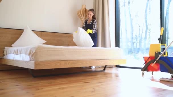 Young woman janitor making bed in living room - Filmagem, Vídeo