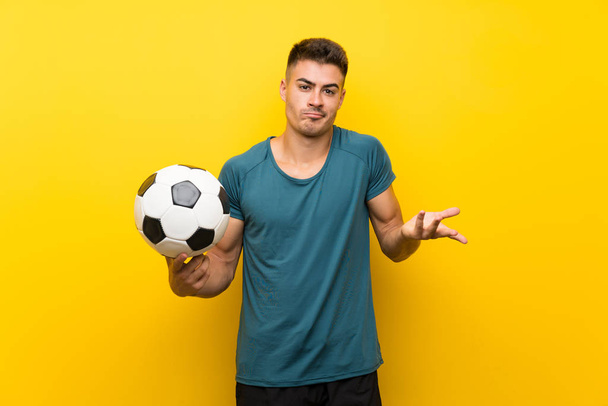 Bonito jovem jogador de futebol homem sobre fundo amarelo isolado fazendo gestos de dúvidas ao levantar os ombros
 - Foto, Imagem