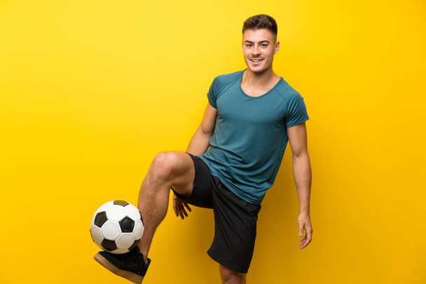 Fešák mladý fotbalista muž přes izolované žluté pozadí - Fotografie, Obrázek