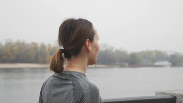 Beautiful woman athlete drinking water from bottle after outdoor exercises. Sports woman drinking isotonic after running. Female runner doing hard workout training in downtown in fog, rear view - Filmmaterial, Video