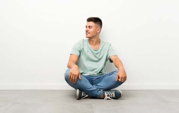 Young handsome man sitting on the floor looking to the side - Photo, Image