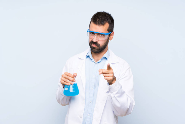 Young scientific holding laboratory flask over isolated background frustrated and pointing to the front - Photo, Image