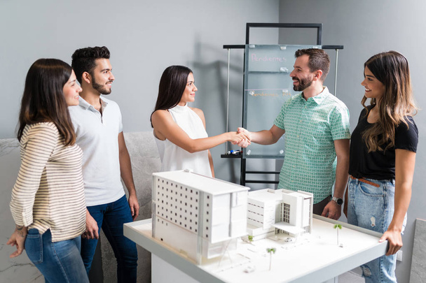 Business partners shaking hands with engineer by architectural model in meeting - Φωτογραφία, εικόνα