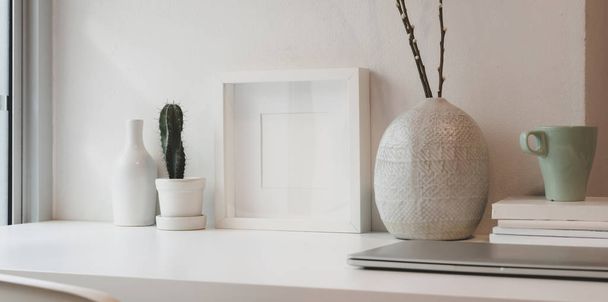Cadre blanc vierge et pot en céramique sur une table blanche contre le mur blanc avec espace de copie
 - Photo, image