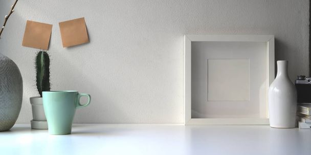 Blank white frame and ceramics jar on a white table against the white wall with copy space - Foto, Imagen