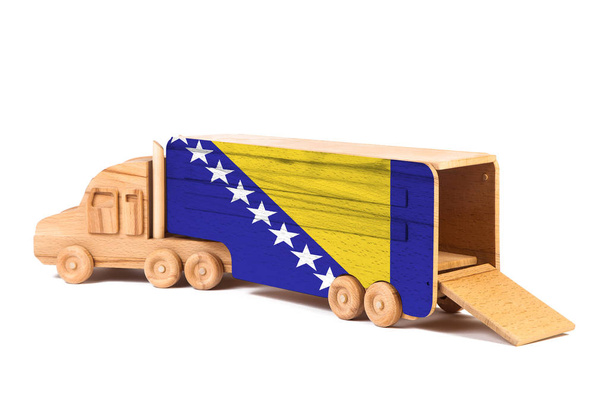 Close-up van een houten speelgoedauto met een beschilderde nationale vlag Bosnië Herzegovina. Het concept van export-import, transport, nationale levering van goederen  - Foto, afbeelding