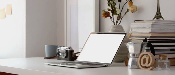 Espaço de trabalho mínimo com computador portátil, câmera, material de escritório e vaso de rosas secas na mesa branca
  - Foto, Imagem