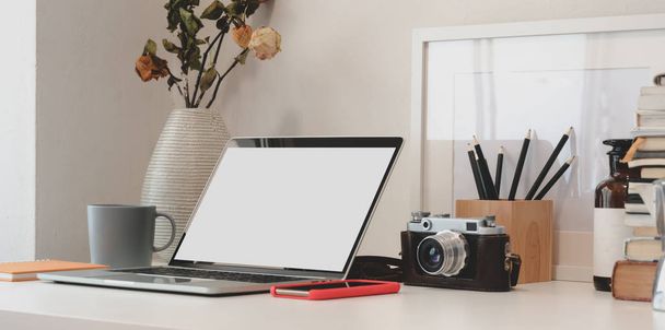 Minimalna przestrzeń robocza z laptopem, kamerą, materiałami biurowymi i suchym wazonem z róż na białym stole  - Zdjęcie, obraz