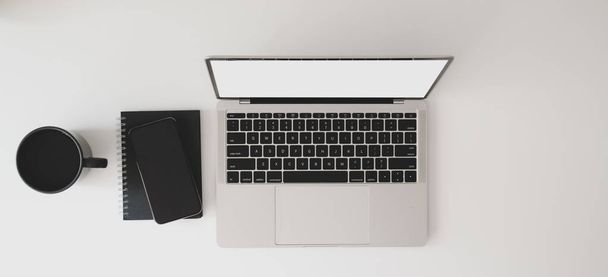 ラップトップコンピュータ、ノートブック、白いテーブルの上のコーヒーカップと現代のワークスペースのトップビュー  - 写真・画像