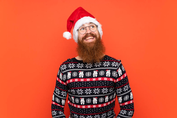 Christmas man with long beard over isolated red background looking up while smiling - Φωτογραφία, εικόνα
