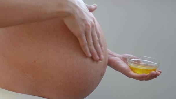 Κοντινό πλάνο ενός έγκυου κοριτσιού που τρίβει λάδι από ραγάδες στο δέρμα της κοιλιάς της. - Πλάνα, βίντεο