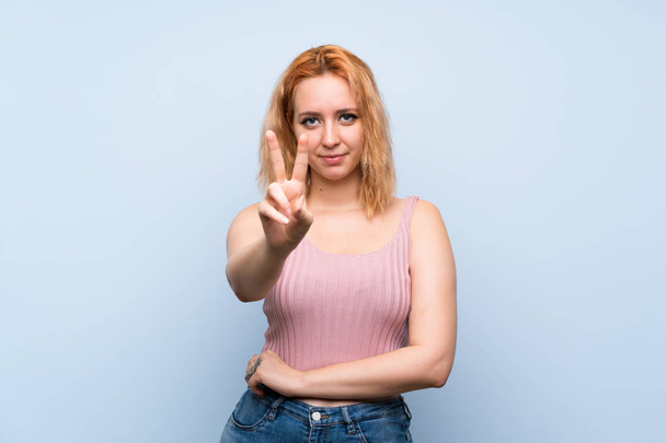 Young woman over isolated blue background smiling and showing victory sign - Photo, Image