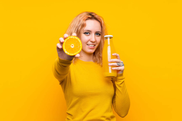 Jonge vrouw met een oranje over geïsoleerde gele achtergrond - Foto, afbeelding