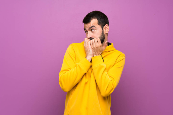 Jóképű férfi sárga pulóverben ideges és ijedt kezek szájba vételétől. - Fotó, kép