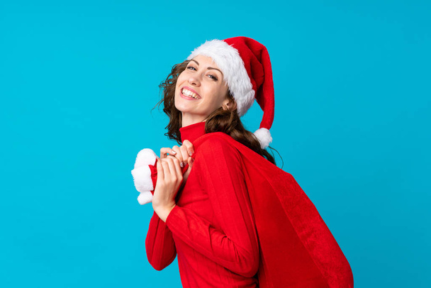 Κορίτσι με χριστουγεννιάτικο καπέλο κρατώντας μια χριστουγεννιάτικη τσάντα γεμάτη δώρα σε απομονωμένο φόντο - Φωτογραφία, εικόνα