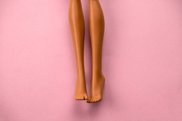 close-up van gladde benen van een plastic speelgoedpop op een zachte roze achtergrond - Foto, afbeelding