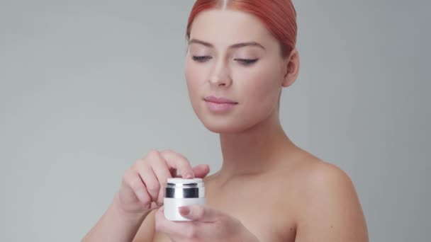 Studio portrait of young, beautiful and natural redhead woman applying skin care cream. Face lifting, cosmetics and make-up. - Video, Çekim