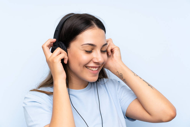 junge Frau hört Musik vor isoliertem blauen Hintergrund - Foto, Bild