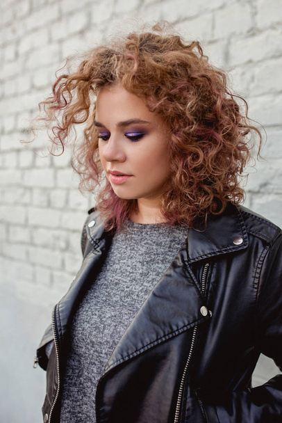 portrait of young beautiful redhead woman with curly hair on white bricks wall background. Film stylization - Zdjęcie, obraz