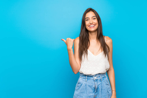 Young woman over isolated blue background unhappy and pointing to the side - Photo, Image