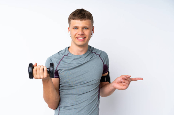 Fiatal sportember súlyemelés felett elszigetelt fehér fal meglepett és mutogató ujj oldalra - Fotó, kép