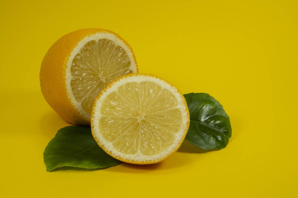 Citrons coupés en deux avec des feuilles vertes sur jaune
 - Photo, image