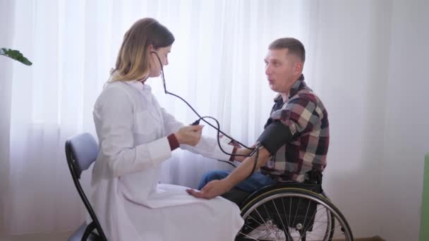 Arztbesuch, medizinisches Personal misst den Druck eines Mannes im Rollstuhl und kümmert sich um den Patienten - Filmmaterial, Video