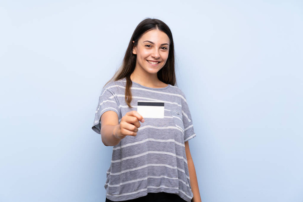 Giovane donna bruna su sfondo blu isolato in possesso di una carta di credito
 - Foto, immagini