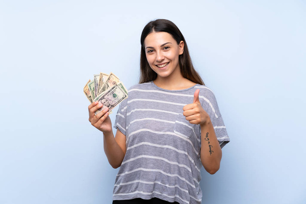 Jeune femme brune sur fond bleu isolé prenant beaucoup d'argent
 - Photo, image