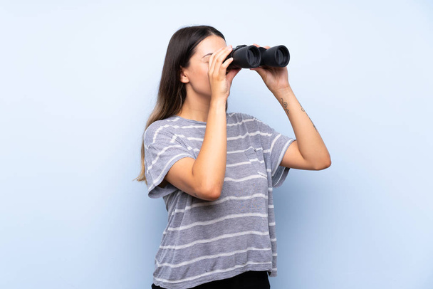 Giovane donna bruna su sfondo blu isolato con binocolo nero
 - Foto, immagini