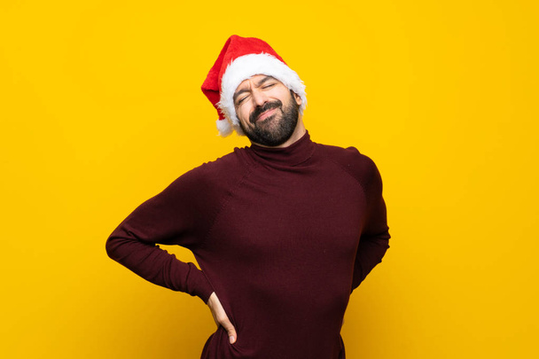 Человек в рождественской шляпе на изолированном желтом фоне страдает от боли в спине за то, что сделал усилие
 - Фото, изображение