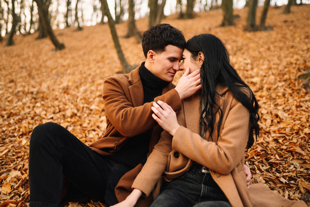 stilvolles junges Paar im Freien an einem schönen Herbsttag im Wald. Ein verliebtes junges Paar hält Händchen und spaziert an einem Herbsttag durch einen Park. das Konzept von Jugend, Liebe und Lebensstil. - Foto, Bild