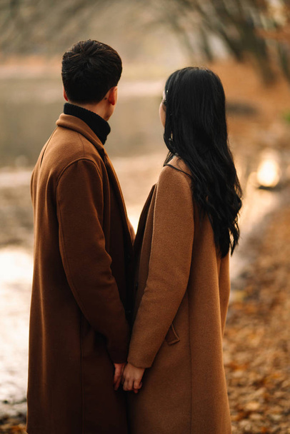 stilvolles junges Paar im Freien an einem schönen Herbsttag im Wald. Ein verliebtes junges Paar hält Händchen und spaziert an einem Herbsttag durch einen Park. das Konzept von Jugend, Liebe und Lebensstil. - Foto, Bild